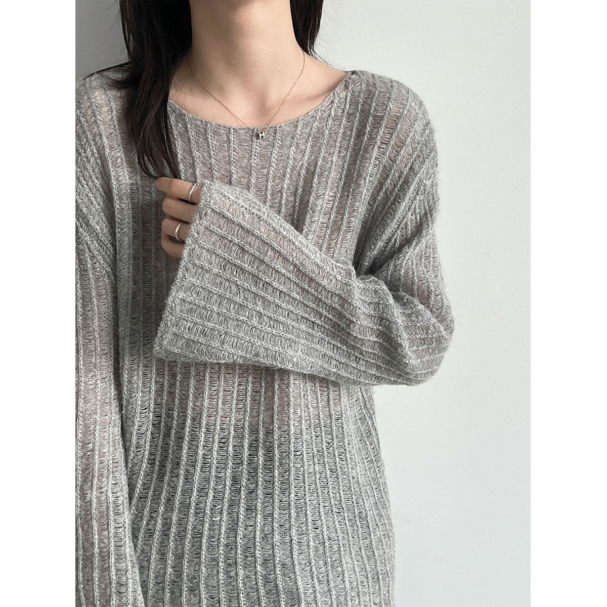 Model wearing a gray open-knit sweater with flared sleeves